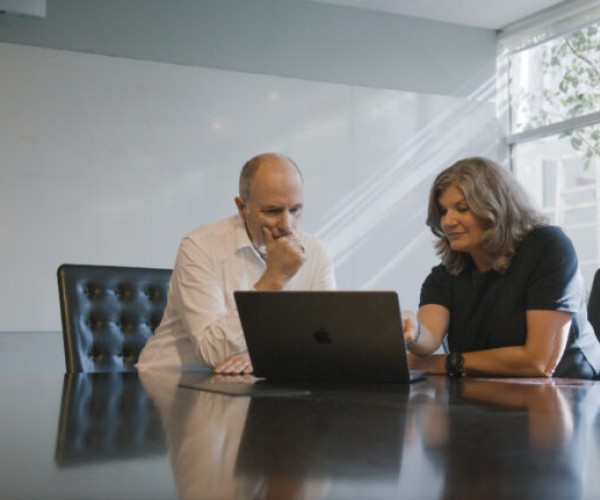 Fiona and Orion Heath’s Chief Medical Officer, Dr Chris Hobson sit with laptop at boardroom table