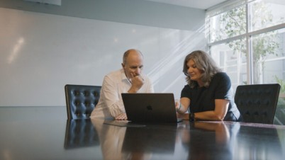 Fiona and Orion Heath’s Chief Medical Officer, Dr Chris Hobson sit with laptop at boardroom table